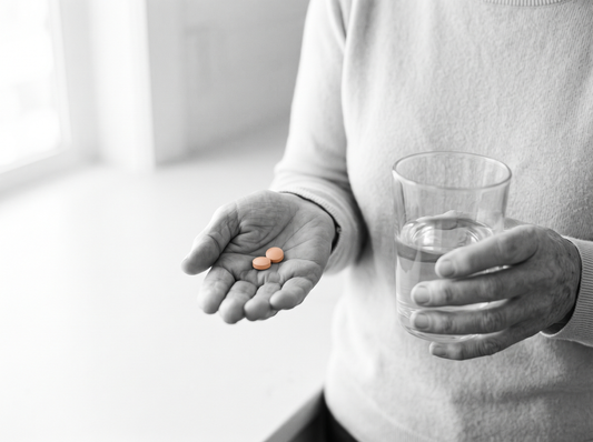 Oudere handen met twee tabletten en een glas water